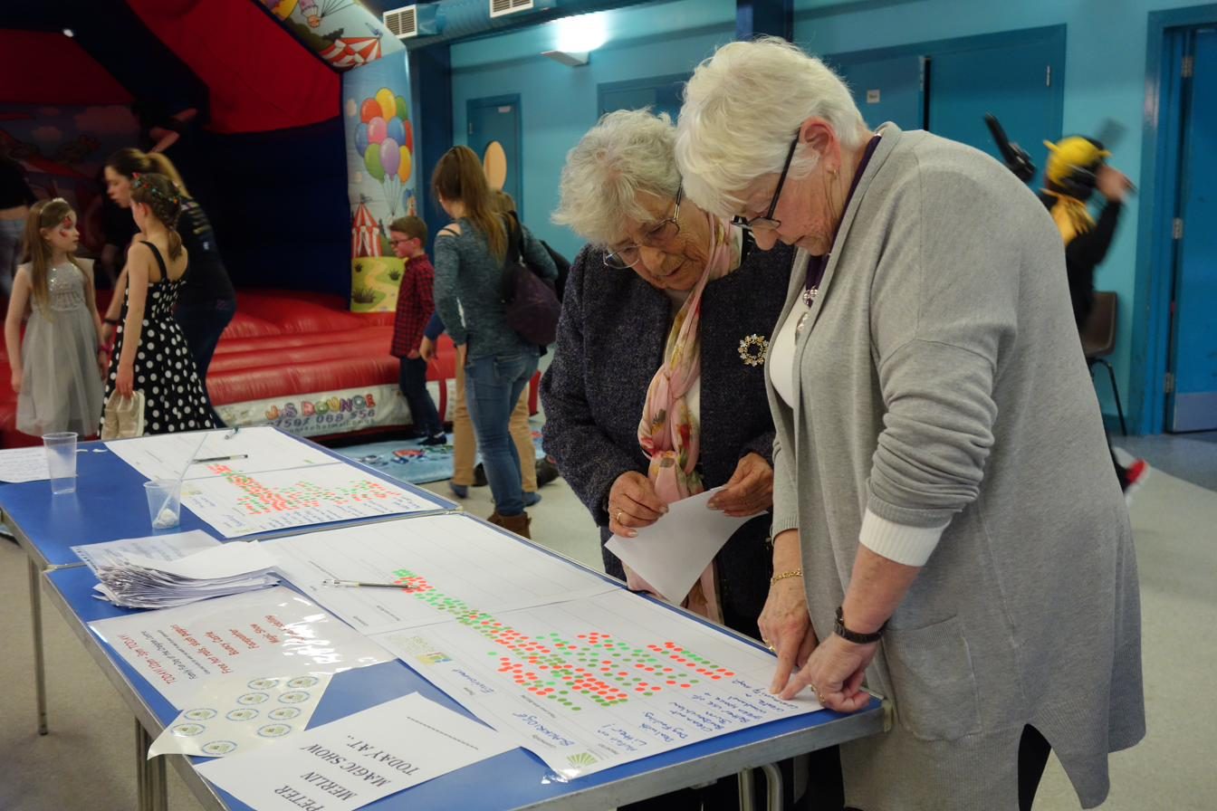 Two residents reading a community voting board covered in red and green sticker dots