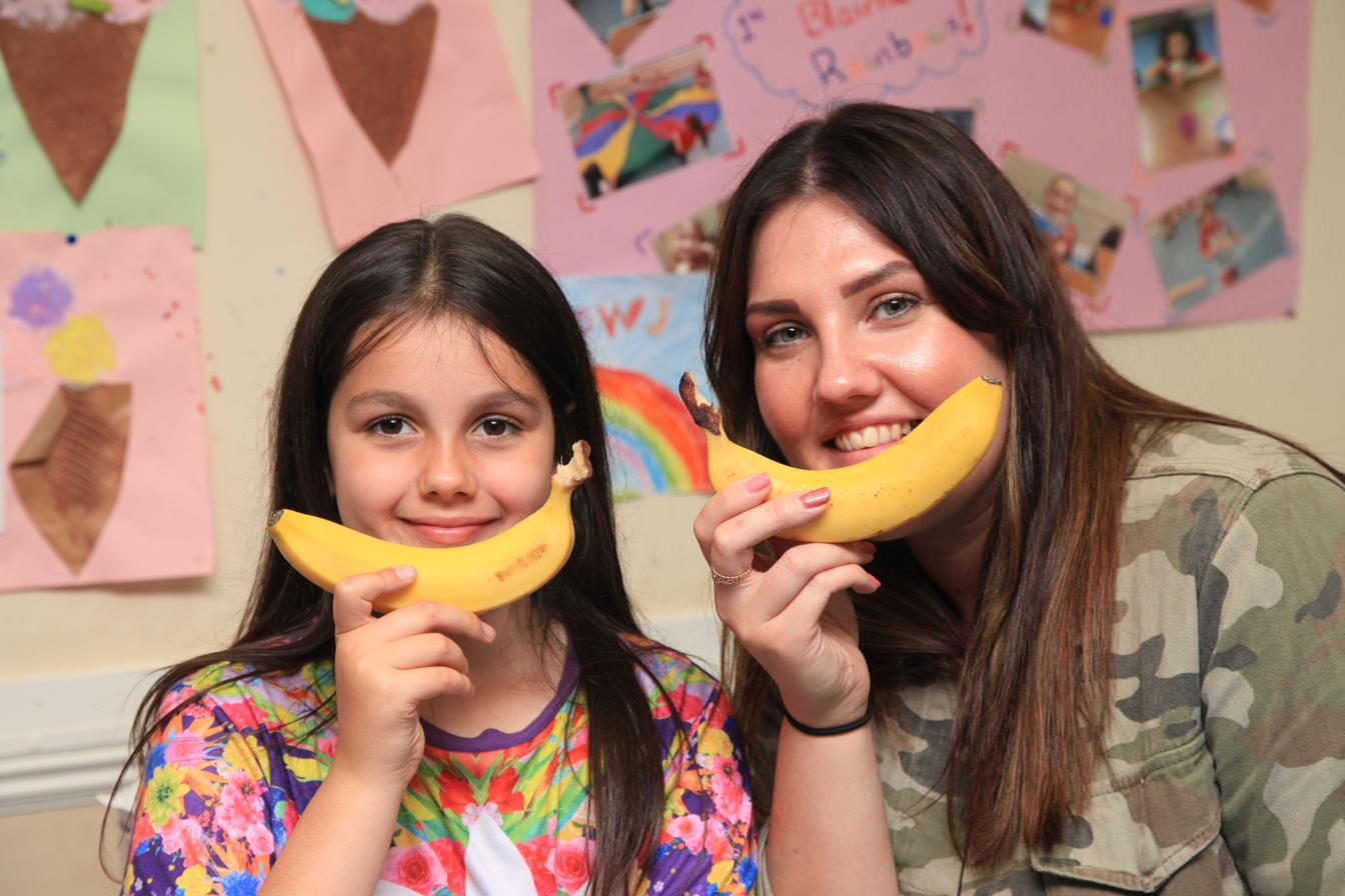 A support worker and a young girl laughing together, holding bananas as smiles